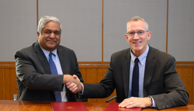 men shake hands sitting behind table