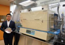 Graduate student Jiadi Zhu holding an 8-inch CMOS wafer with molybdenum disulfide thin film. On the right is the furnace the researchers developed